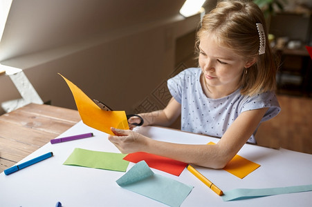 丰富多彩的玩小姑娘在桌子上剪彩纸小孩在桌边剪彩纸艺术学校的创意课上年轻画家愉快爱好乐童年小女孩剪彩纸子在工作间调色板背景图片