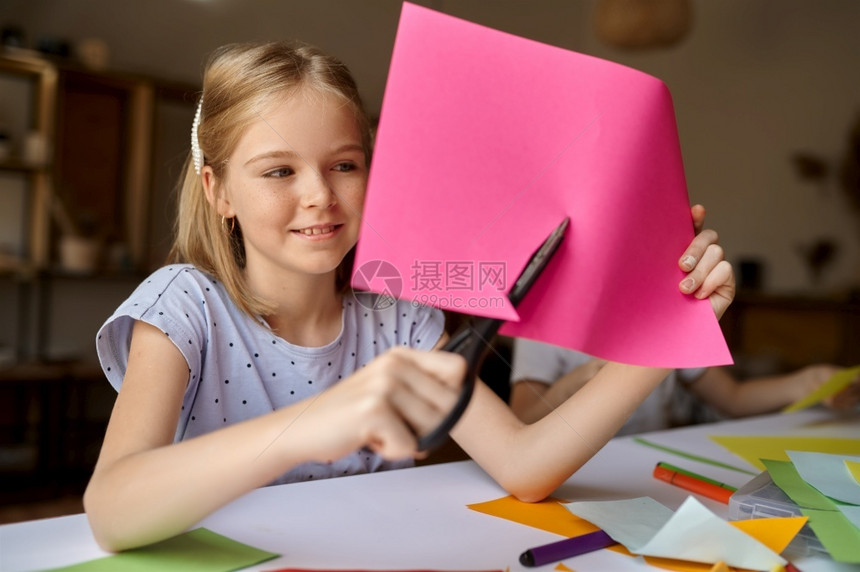 小姑娘在桌子上剪彩纸小孩在桌边剪彩纸艺术学校的创意课上年轻画家愉快爱好乐童年小女孩剪彩纸子在工作间室艺年轻的图片