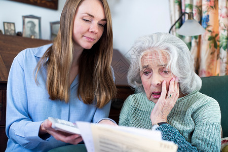 帮助担心债务与帐单和纸面工作的妇女帮助担忧老年邻居金融文档个人的图片