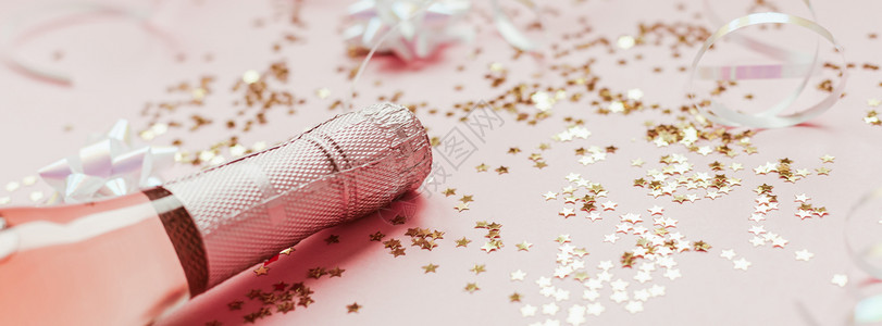瓶子圣诞或新年配有玫瑰香槟和金光闪的星彩蛋白在粉色面背景上边观党庆祝会创意概念的歌唱会灯问候背景图片