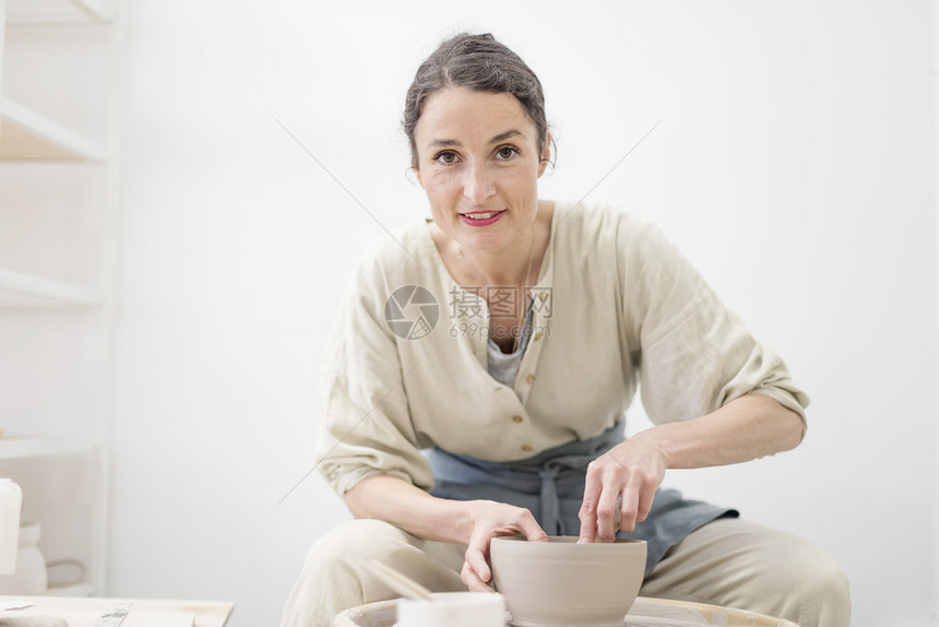 经过才华横溢成人年轻女坐在桌边工作室制造粘土或陶瓷杯图片