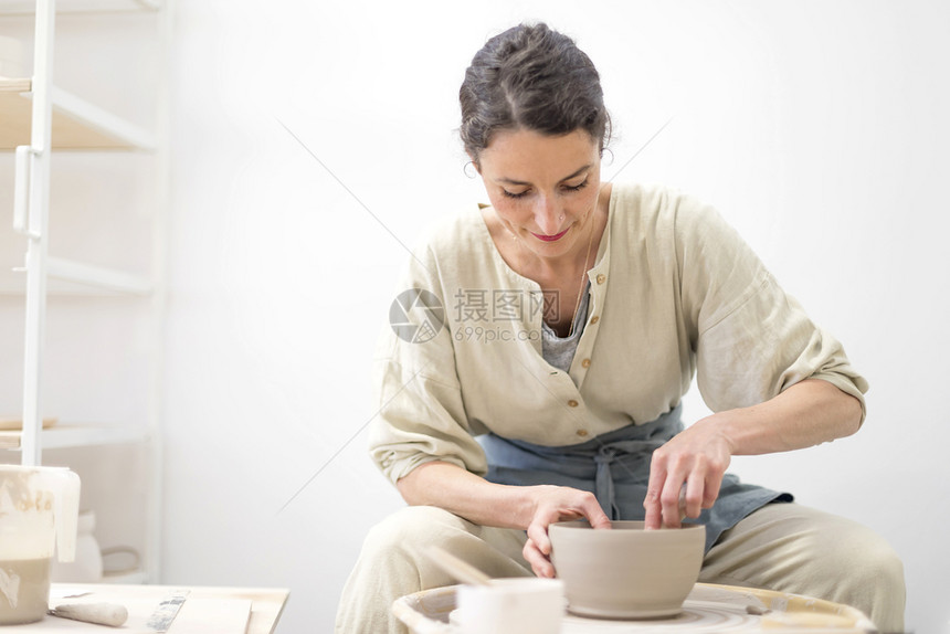 年轻女坐在桌边工作室制造粘土或陶瓷杯年轻的女士商业图片