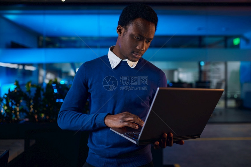一名经理在夜间办公室用笔记本电脑工作男人黑暗商业中心内地背景现代工作场所商人植物现代的图片