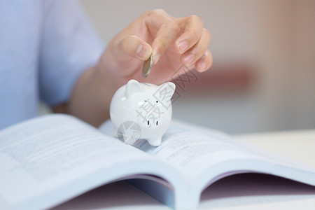 毕业学生在书本上的白猪银行里放一枚硬币为教育省钱贷款了设计图片
