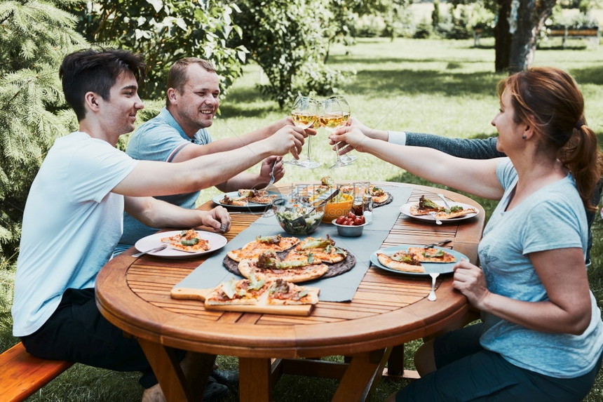 积极的盛宴超过朋友在夏季野餐室外晚宴期间在一家庭花园里做吐司朋友在一家庭花园里做吐司在夏日野餐室外晚宴中朋友在后院果园里的一个用图片