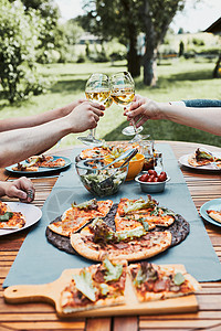 吐司披萨葡萄酒粘合朋友在夏季野餐室外晚宴期间在一家庭花园里做吐司朋友在一家庭花园里做吐司在夏日野餐室外晚宴中朋友在后院果园里的一个用披萨背景
