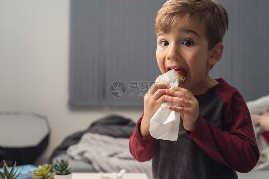 包裹在餐巾纸或糕饼中吃晚餐三明治的幼童肖像坐在张开的嘴前吃饭一边看着镜头前视线站立笑声保持童年图片