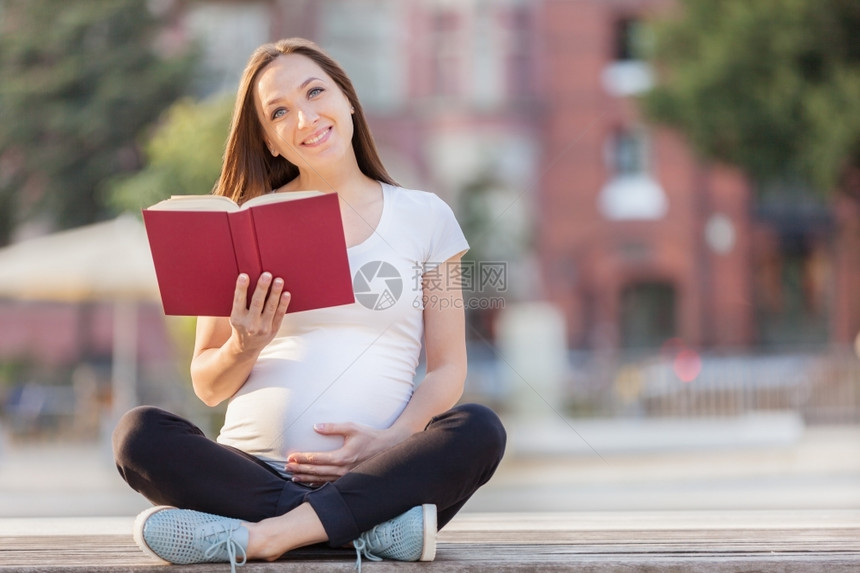 肚子母CaucasianBrunette孕妇在长椅上阅读这本书的照片银行图片