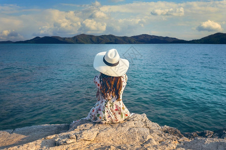 年轻女士坐在岩石的顶端看着海边的古老音调天空旅行相同图片