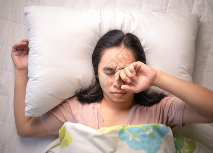 睡觉恨移动的亚裔年轻女子睡着清晨在床上敲闹钟图片