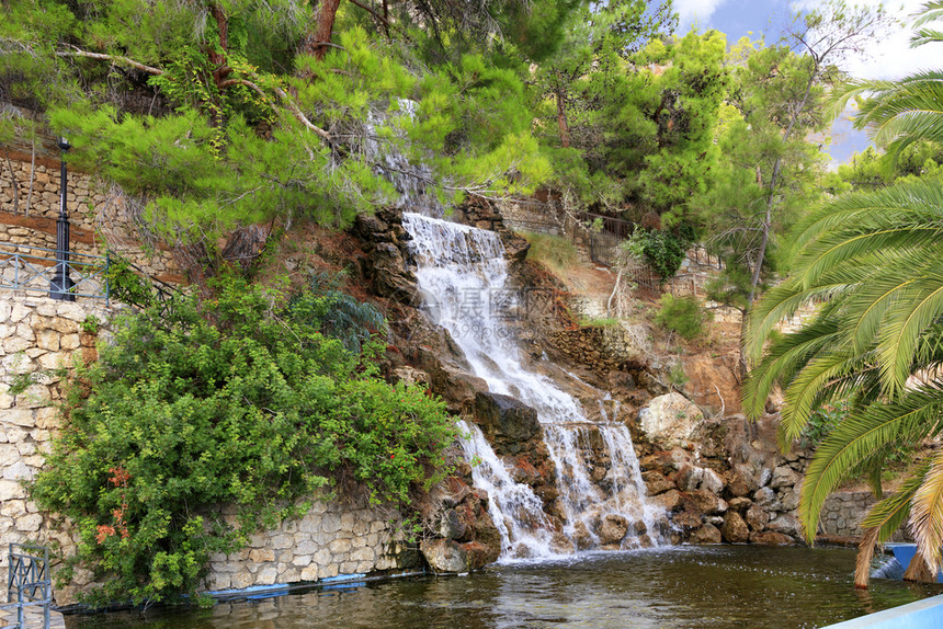 旅行河来自氡水泉的大瀑布从山脚下的大石头上流在希腊Loutraki公园的绿色地中海松树和棕榈之间希腊中图片