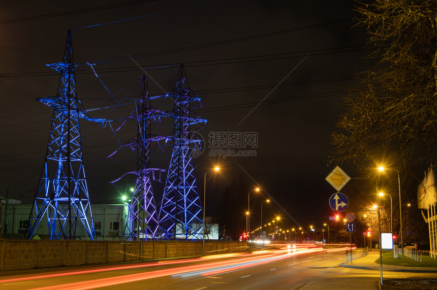 活力极传送高电压塔晚上以蓝色和紫灯光照亮高电压塔街道灯照在长射期的地面前方图片