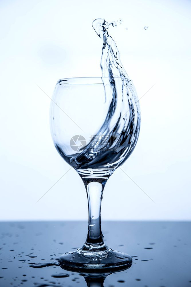 流动溅起在黑玻璃桌上的一杯清洁饮用水中喷洒花气泡图片