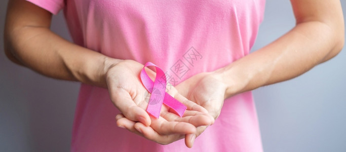 穿粉红T恤的妇女手握粉丝带预防癌症概念图片