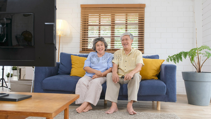 女士长椅在家中客厅看电视时持遥控器的老年亚裔夫妇在有幸福老年人退休和生活正常的安居室观看电视图片