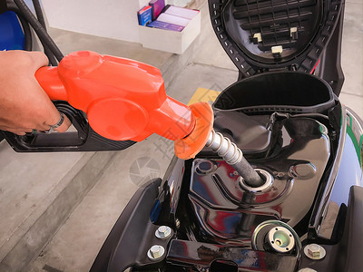 笔芯泵紧闭持有燃料撒油机的雇员手并将苯基燃料添加到摩托车配额燃料罐中加油背景图片