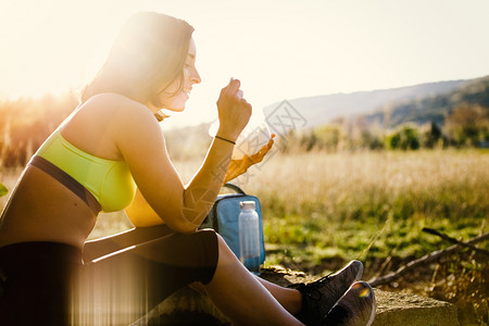 微笑日落时在田里吃健康午餐的年轻运动妇女野餐酷袋图片