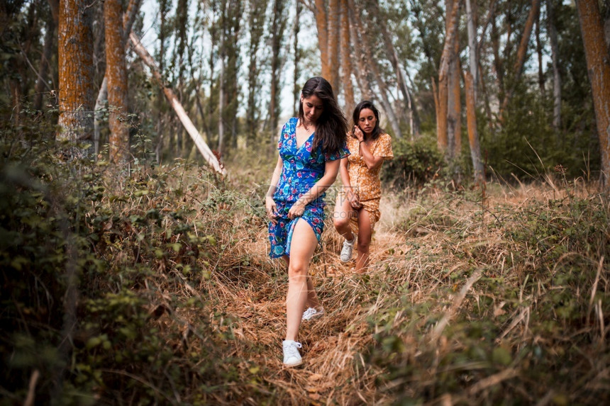 爱抚幸福两名年轻女者穿着长裙在树林中手牵行走图片