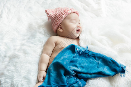可爱的保护皮肤新生儿30天大男孩在白床上笑着微在蓝包布下放松感到快乐图片