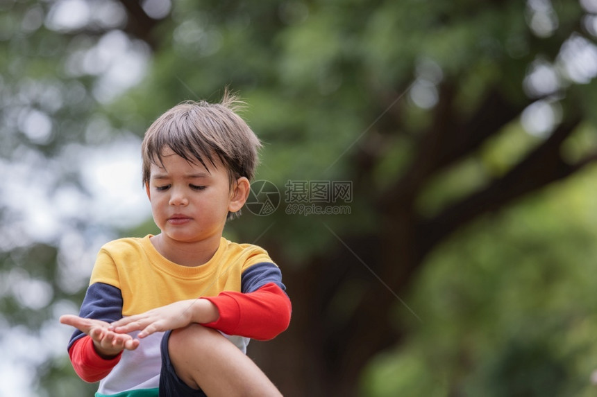 攀登一名男孩在公园的树枝上坐着身彩色鲜亮衣服并按摩由爬树引起的手掌一种扭伤图片