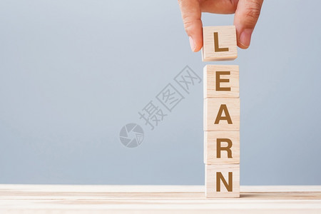 learn木制的商人手握立方块LEARN在桌边背景学习教育知识学习和智慧上写有商业文字信息沟通背景