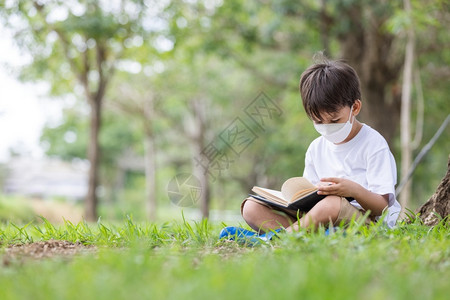 白种人患病的一名身戴卫生面具的白人男孩独自坐在一棵树下阅读本书孩子们图片