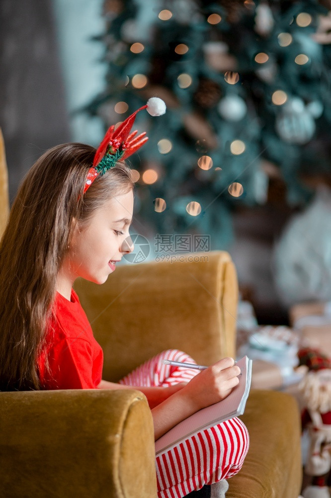 沙发上头戴圣诞装饰的可爱女孩写信图片
