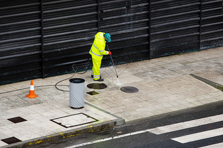 男人铺路在雨季用高压喷水机清理街道人行和高压水式喷机工作图片