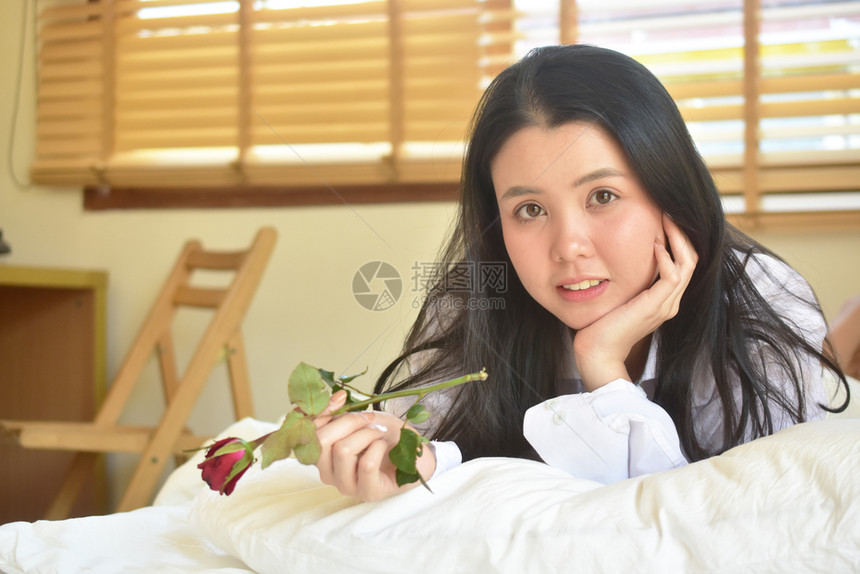 女士美丽容穿着玫瑰的白衬衫在床上卧室年轻女子可爱的微笑在情人节的概念自在图片