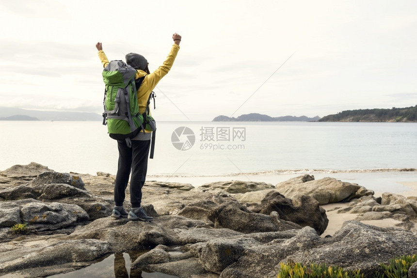 成功探险家海滩怀着背包和手举起的女享受着美丽的海岸清晨风景图片