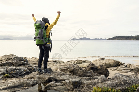 成功探险家海滩怀着背包和手举起的女享受着美丽的海岸清晨风景图片