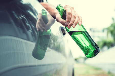 男瘾君子虐待醉酒男驾驶一辆汽车在路上载着啤酒瓶的车危险醉酒驾驶概念图片
