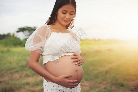 日出时在公园里看着肚子的亚洲孕妇快乐和自豪等待腹部母图片
