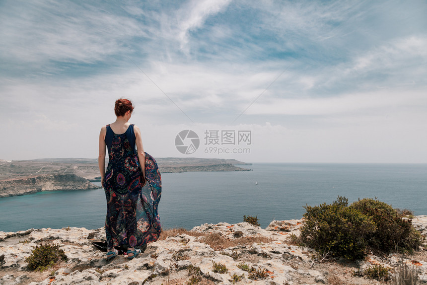 身穿长裙的红发女青年从悬崖边缘穿着长裙子随风而动户外天空自由图片