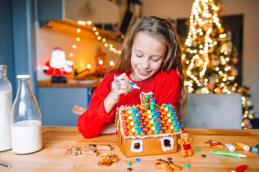 可爱的小女孩装饰着姜饼屋有迷人的美丽厨房有灯光和圣诞树桌子上还有蜡烛圣诞快乐和节日小姑娘在厨房做圣诞姜饼屋在厨房饼干新的幸福图片