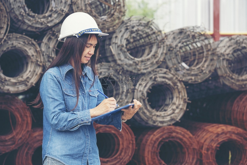 机械作坊女建筑工程师在地身戴安全白色钢帽的建筑工场薪女程师土木带有硬帽子安全头盔的女建筑工程师概念a妇女建筑工程师外部图片