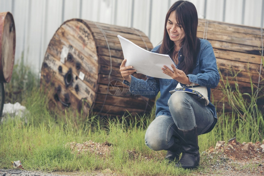 格子人们女建筑工程师在地身戴安全白色钢帽的建筑工场薪女程师土木带有硬帽子安全头盔的女建筑工程师概念a妇女建筑工程师作坊图片