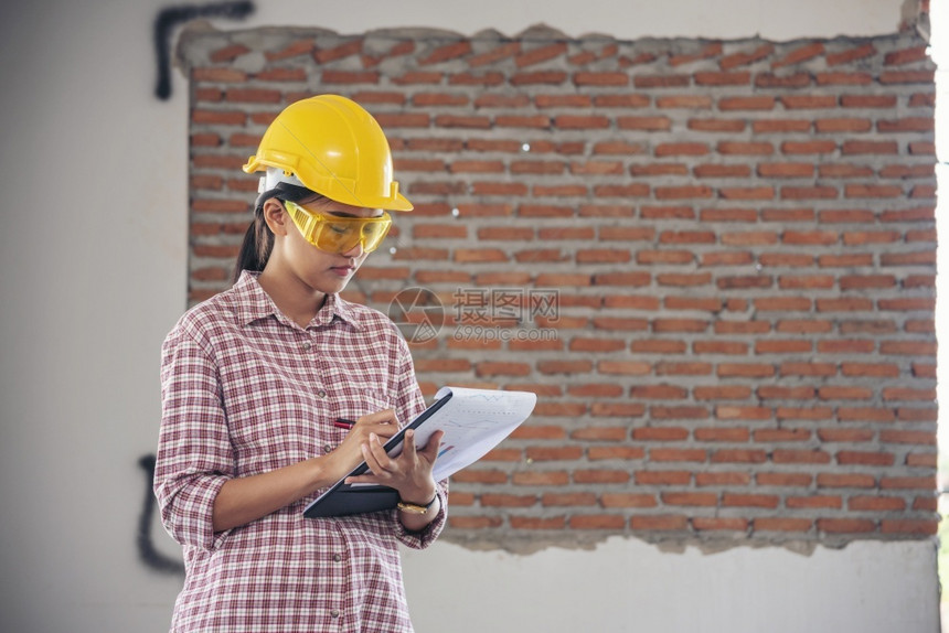穿屋女建筑工程师在地身戴安全白色钢帽的建筑工场薪女程师土木带有硬帽子安全头盔的女建筑工程师概念a妇女建筑工程师机械图片