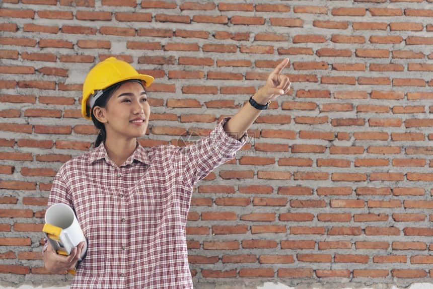 写作女建筑工程师在地身戴安全白色钢帽的建筑工场薪女程师土木带有硬帽子安全头盔的女建筑工程师概念a妇女建筑工程师企业家作坊图片