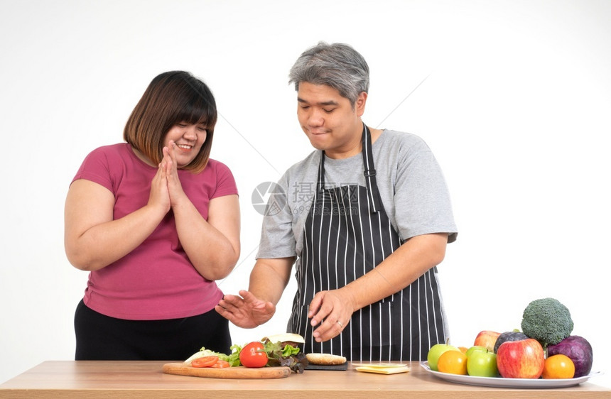 泰国人们快乐的超重夫妇在厨房做汉堡餐室吃一个汉堡A蔬菜放在桌子上幸福的家庭和狂欢饮食的概念享受图片
