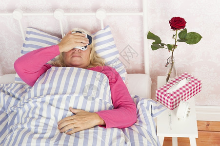 穿粉红色睡衣的女人有眼痛组织和一朵玫瑰床铺着毛巾躺在上成人压力说谎图片