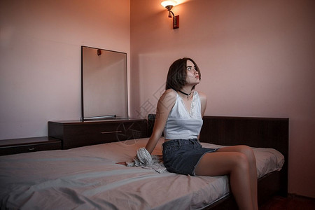 成人吸引的沮丧一个穿短裙子的年轻女孩和白衬衫坐在床上面脸伤感痛又体贴图片