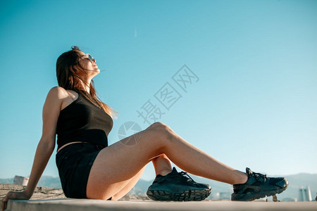 穿着黑色运动鞋短裤和的头发女孩坐在一栋高楼屋顶上阳光冒险高的图片