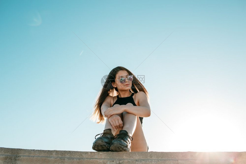 日落旅行白种人穿着黑色运动鞋短裤和的头发女孩坐在一栋高楼屋顶上图片