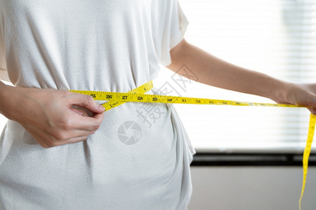年青的亚洲女在吃健康食品后尝试减肥用测量腰部的胶带美丽腹数字图片