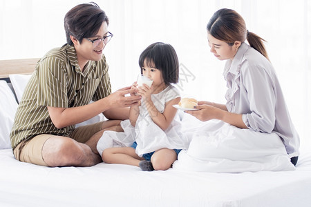 孩子他们的女一个亚洲人的父母每天早上在床为自己的小女儿提供早餐和奶水图片