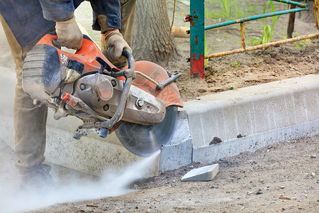 一名工人使用水泥切割机在一个建筑工地用混凝土锯切水泥截断的路面在开放的空间工人中用水泥切碎路面将段割开汽油风险具体的背景