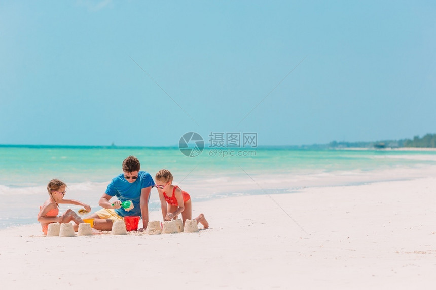 海滨情感父亲和两个女孩在热带海滩上玩沙子父亲和孩在热带海滩做沙城堡家庭在海滩玩具岸线图片