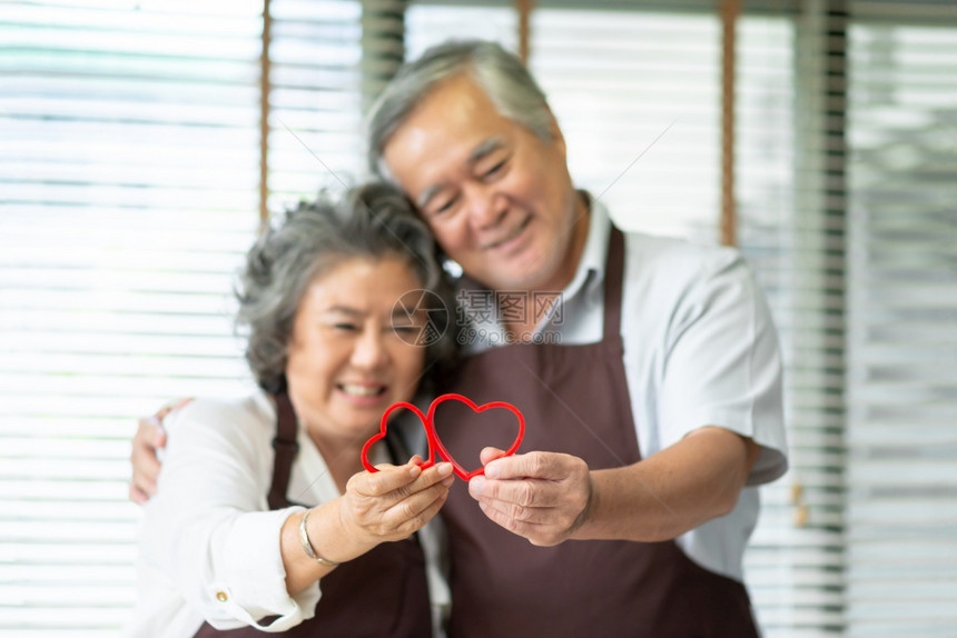 面团穿着棕色围裙的亚洲快乐老年情侣带着红饼干切机在心脏形状一起爱情人节妻子祖母图片
