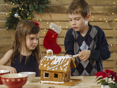 圣诞节的孩子厨房女儿一位年轻兄弟姐妹在圣诞节前夕家里装饰姜饼屋的照片该来自BeableBread背景